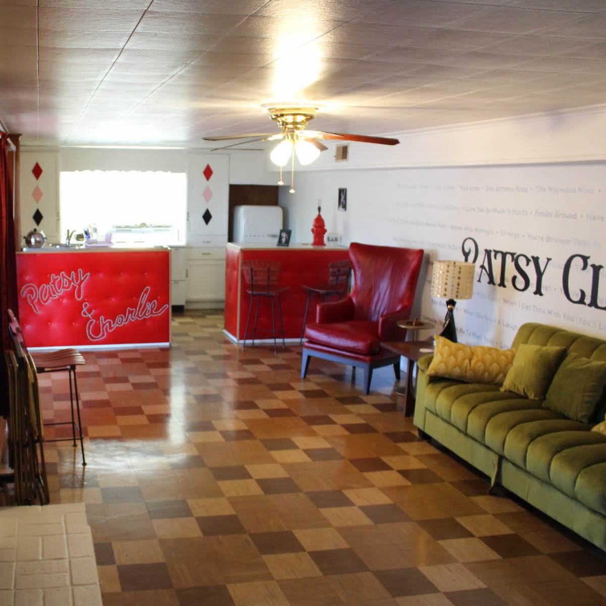 A living space with a green sofa, red chairs, a red kitchen bar, and patterned flooring.