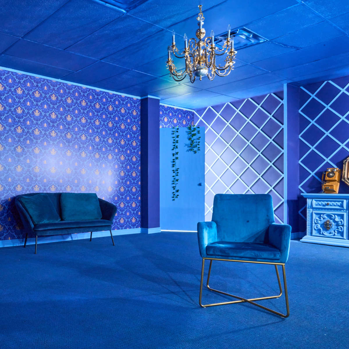 A modern room with blue walls featuring patterned wallpaper, a chandelier above, and two upholstered chairs in contrasting styles.