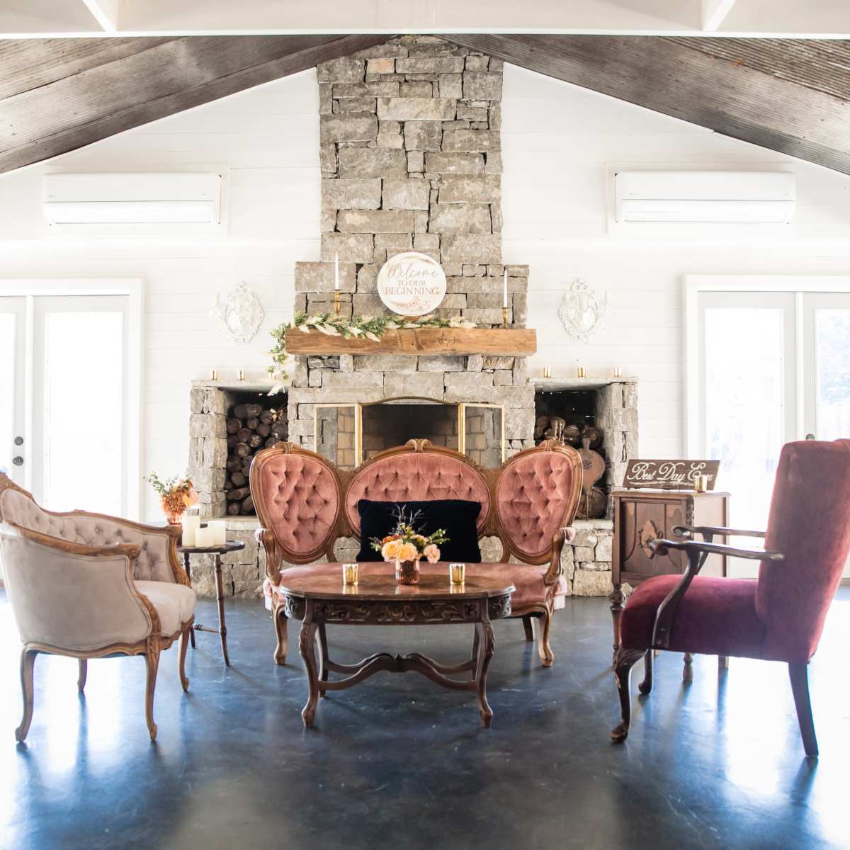 A cozy sitting area features a stone fireplace, a wooden mantel, and various upholstered chairs arranged around a central table.
