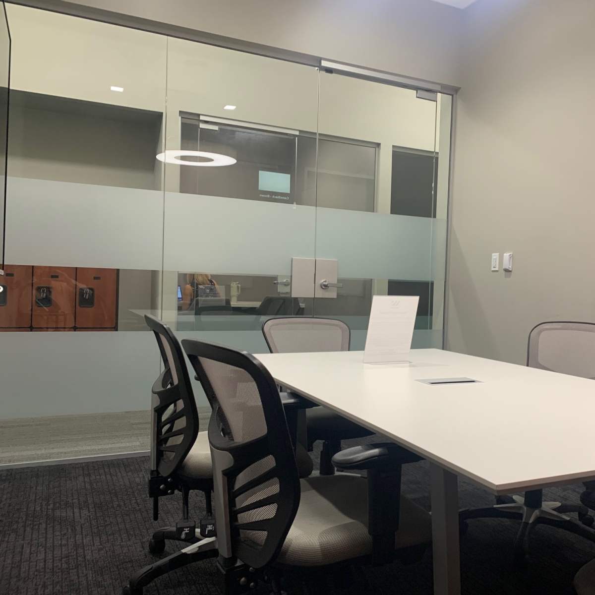 A conference room with a white table, several chairs, a whiteboard, and glass walls.