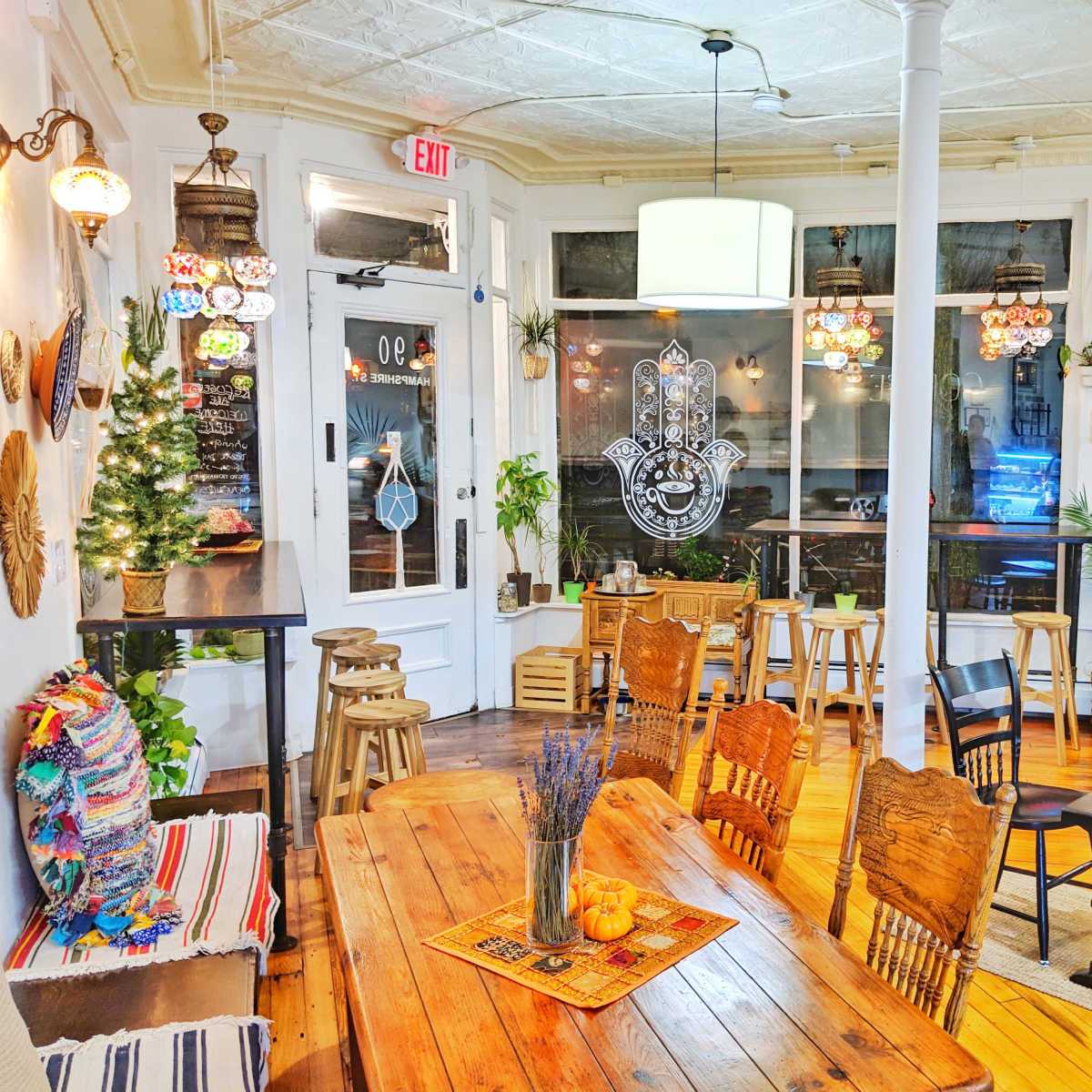 A cozy café interior featuring wooden tables, chairs, and vibrant decor including wall art and plants, with patrons seated at tables.