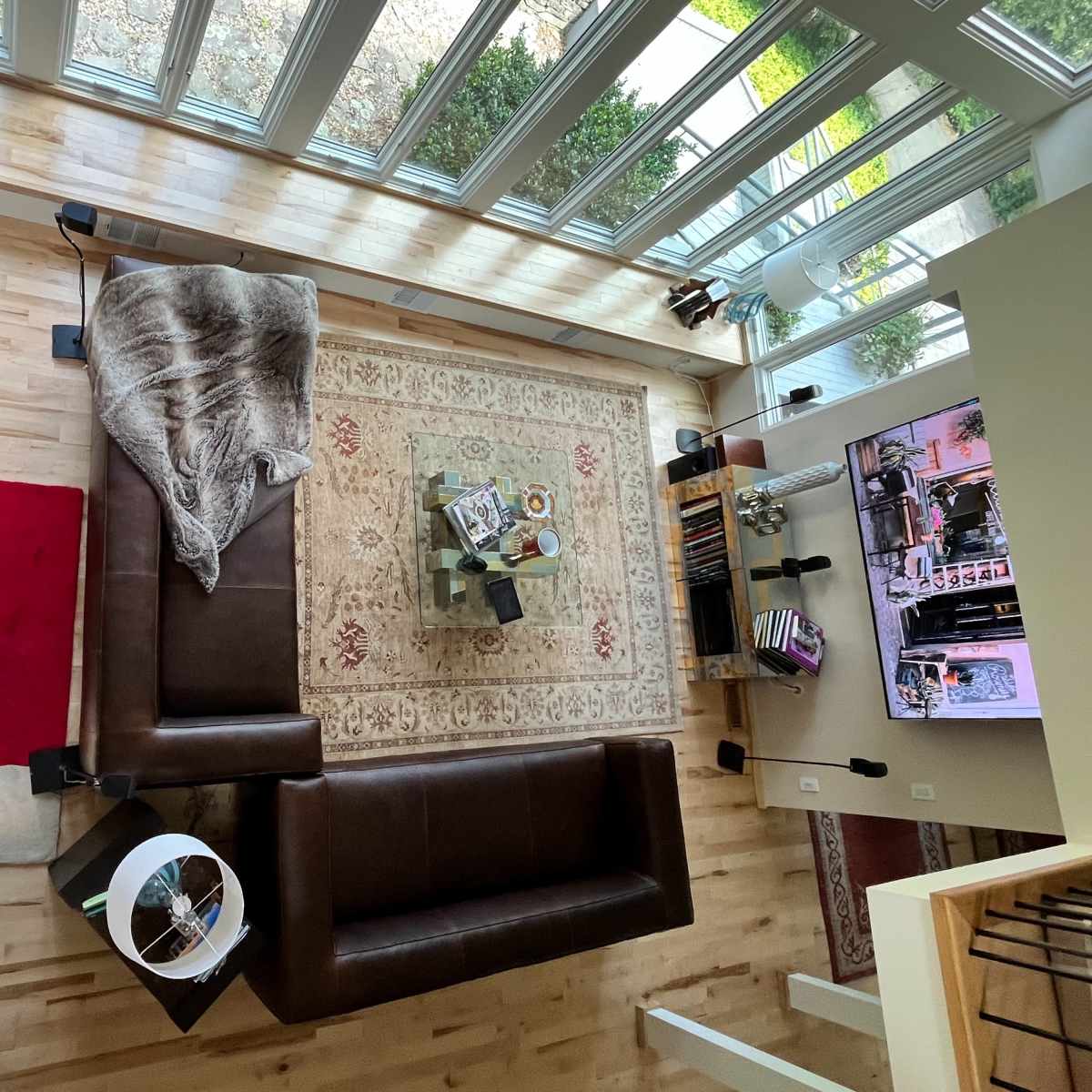 A spacious living room with a large brown sectional sofa, a glass coffee table, and a patterned area rug, all surrounding a bright windowed space.