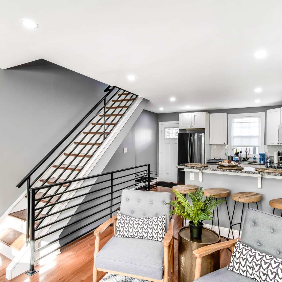 A modern interior with a staircase, a kitchen area, and seating arranged in a living space.