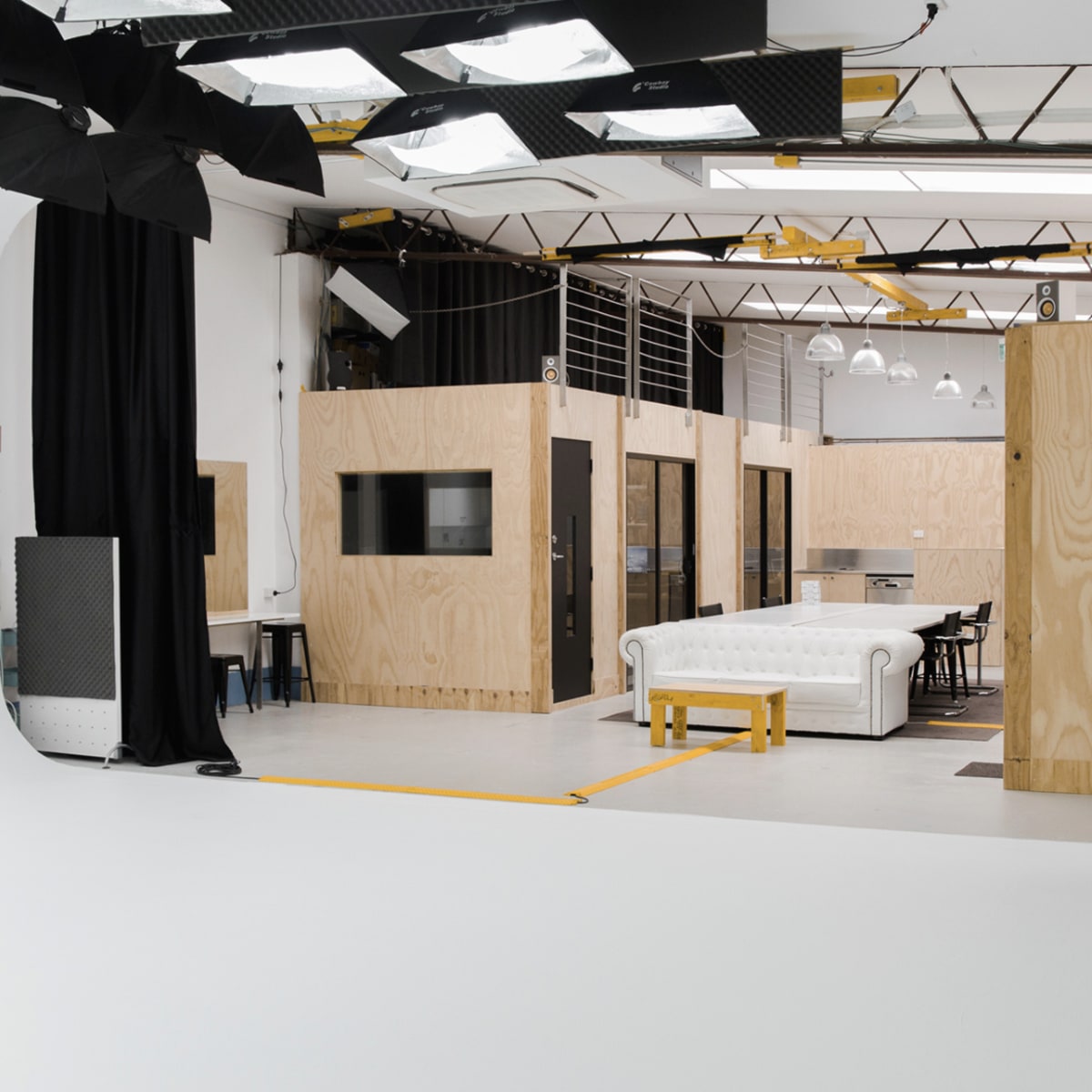 A spacious studio interior featuring wooden partitions, a white couch, and studio lighting equipment.