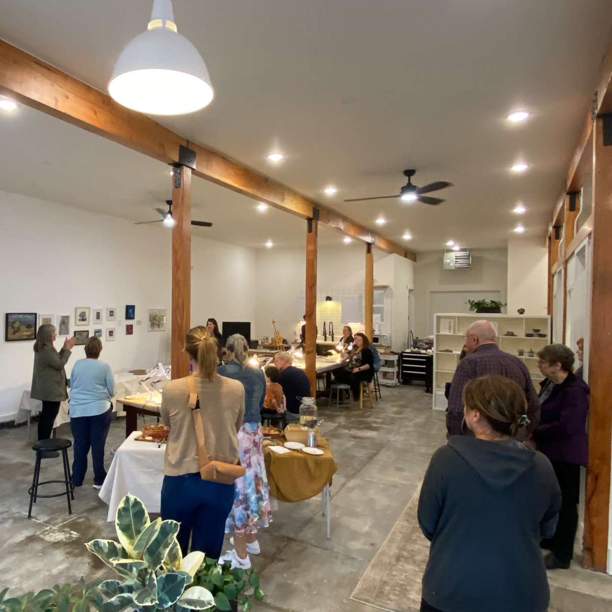A group of people is attending an exhibition in a spacious, well-lit room with wooden beams and various displays along the walls.