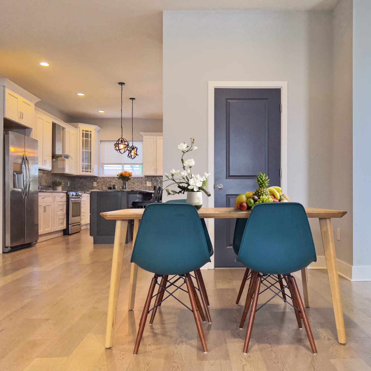 A dining table with blue chairs is positioned near a kitchen featuring white cabinetry and stainless steel appliances.