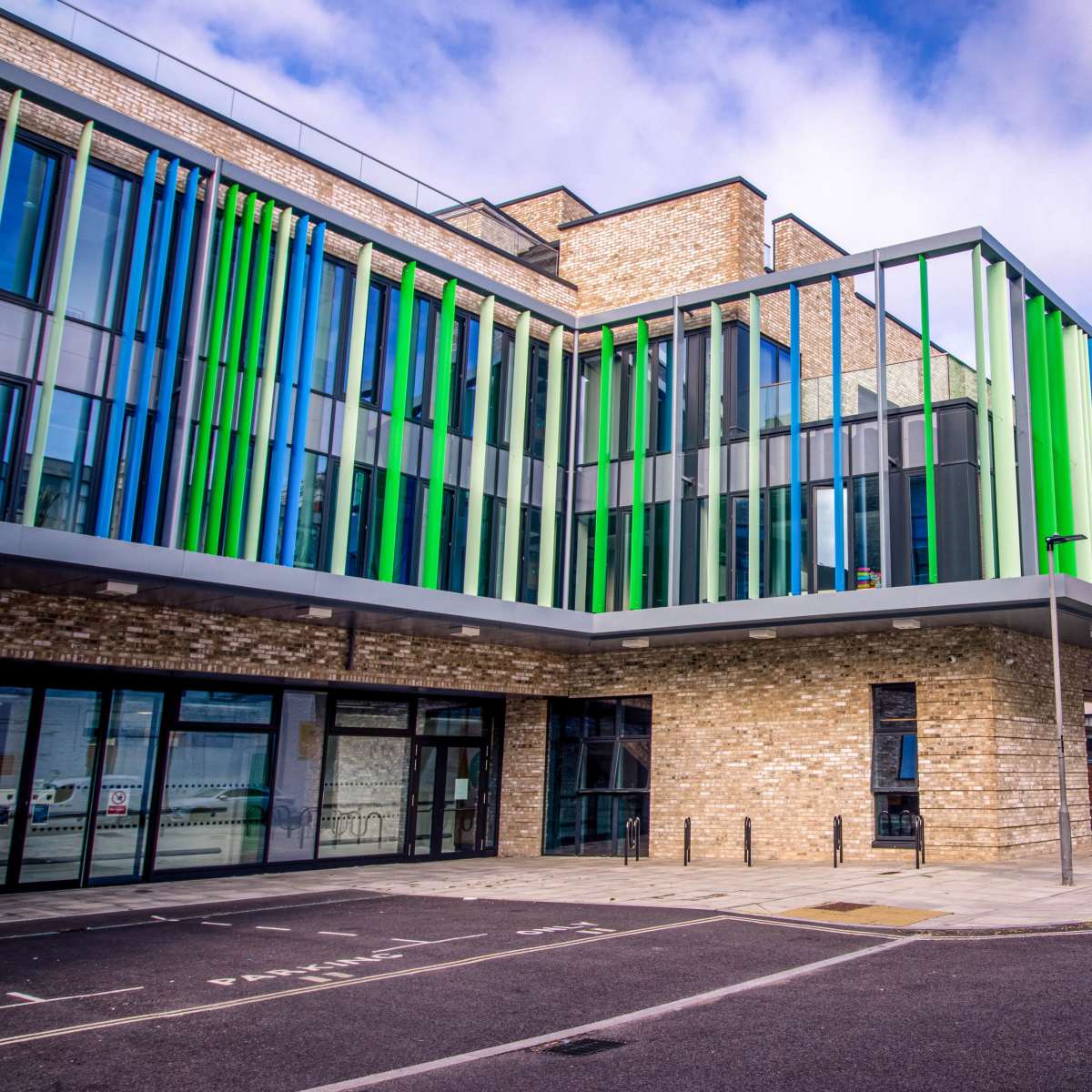 A modern building with colorful vertical glass panels and a brick facade, situated on a street next to a brick factory.