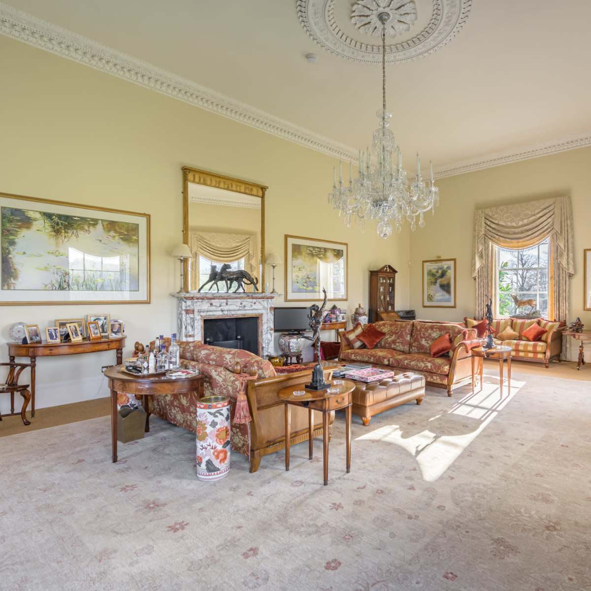 A spacious living room furnished with ornate chairs, a chandelier, and various decorative elements, including framed art and a fireplace.