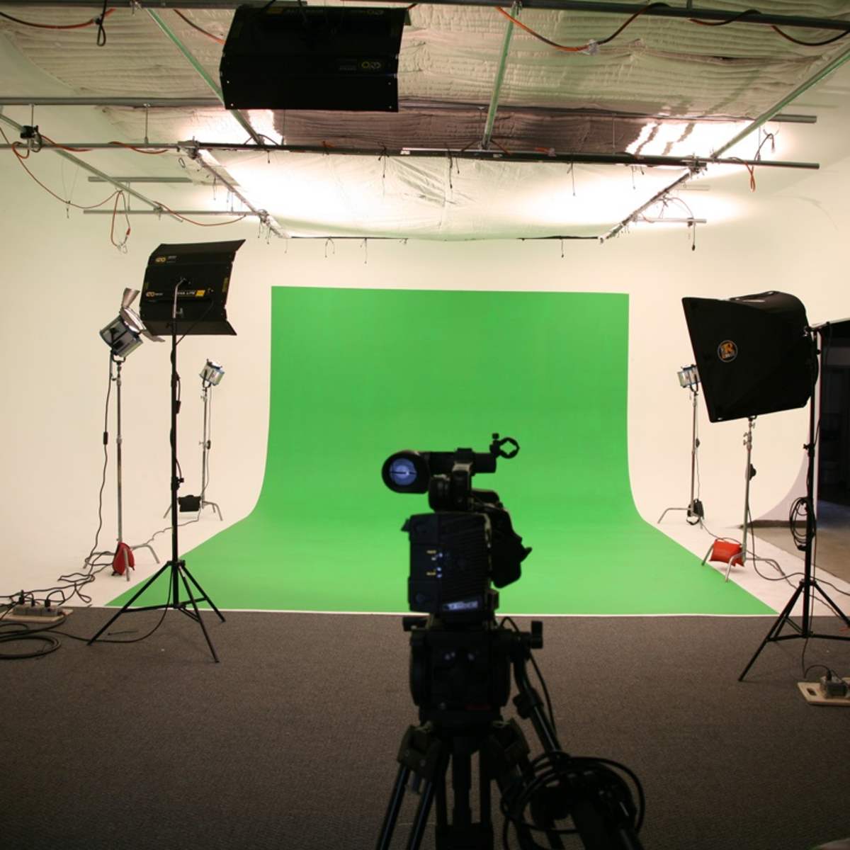 A photography studio with a green backdrop, a camera on a tripod, and studio lights positioned around the setup.
