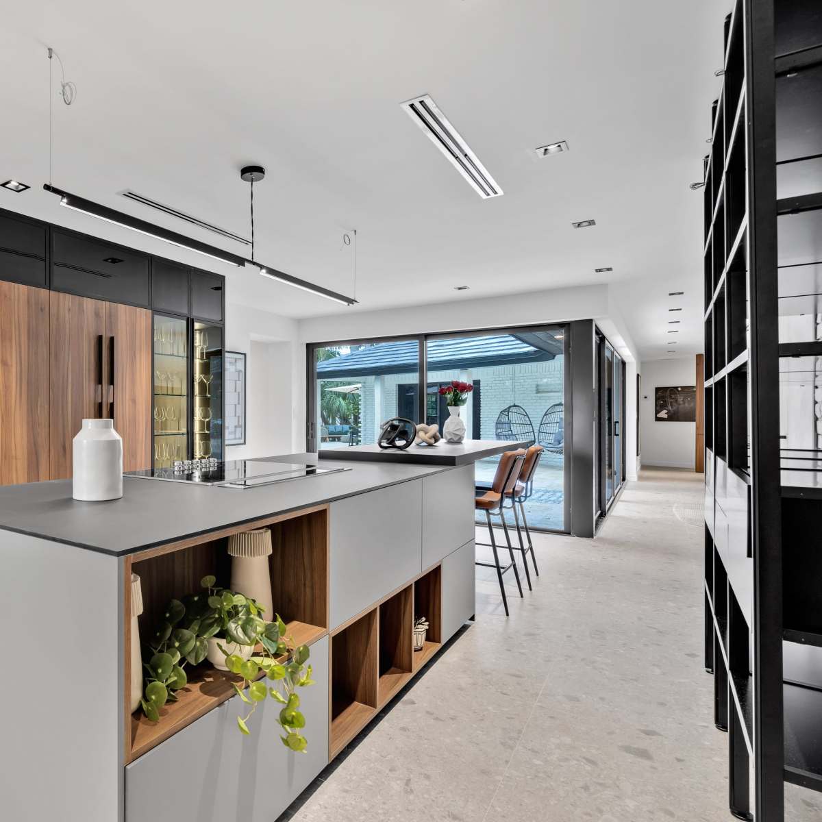 A modern kitchen with a central island, sleek cabinetry, and large windows that open to an outdoor area.