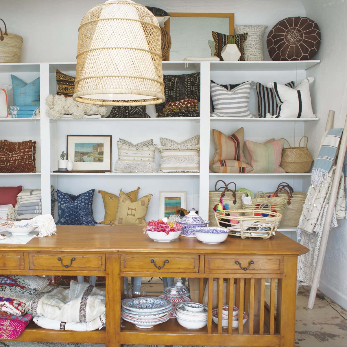 A well-organized retail space showcases various decorative pillows, woven baskets, and ceramic bowls on shelves and a central wooden table.