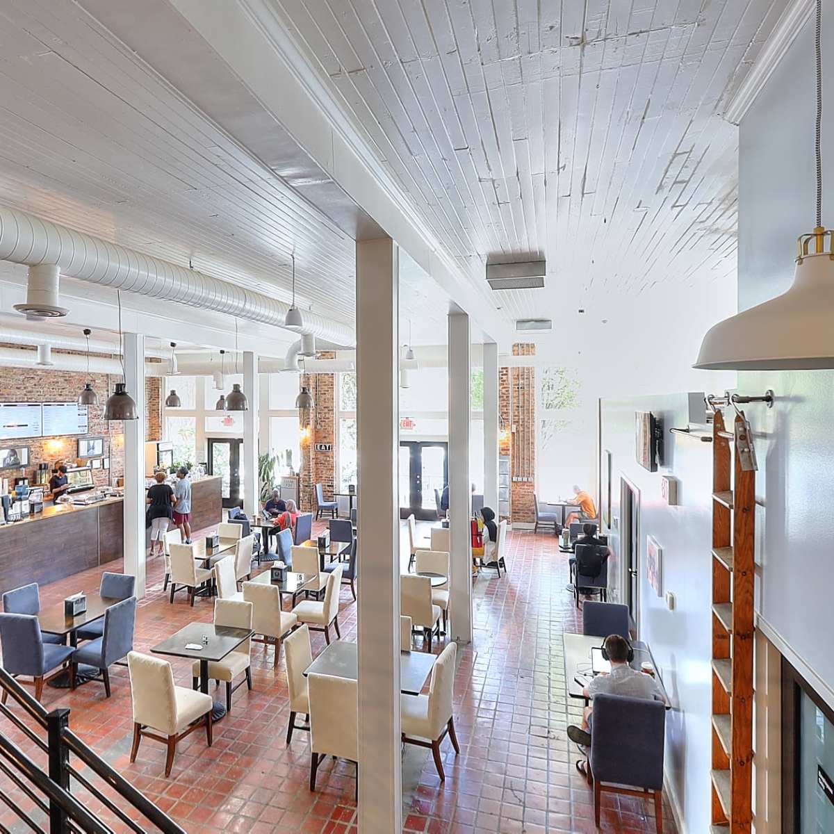 A spacious café with a modern design, featuring a counter at the back and tables arranged throughout the area.