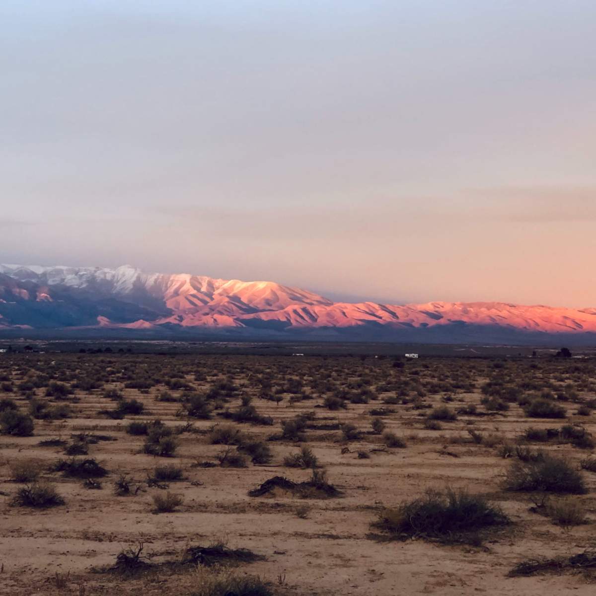 A barren landscape features a range of mountains bathed in warm light, with sparse vegetation scattered across the arid land.