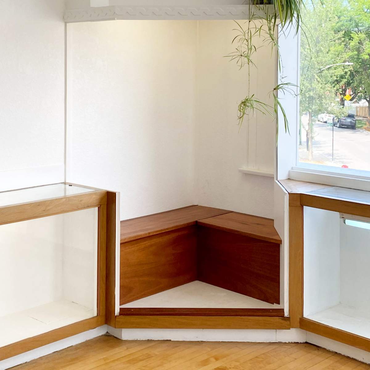 A bright, minimalistic corner of a room with a wooden bench and a window featuring a plant.