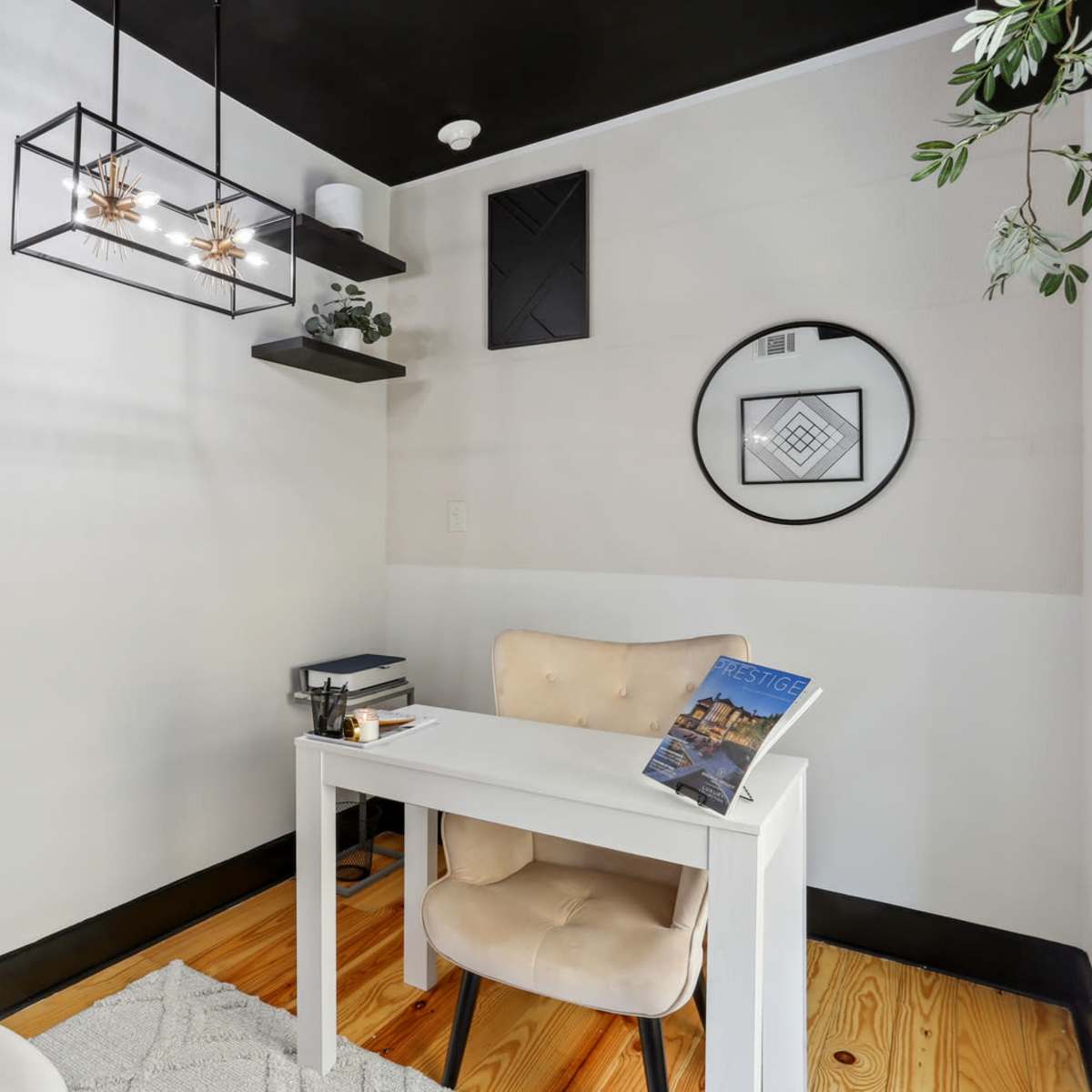 A modern home office with a small white desk, a chair, and decorative elements like a hanging light fixture and plants.