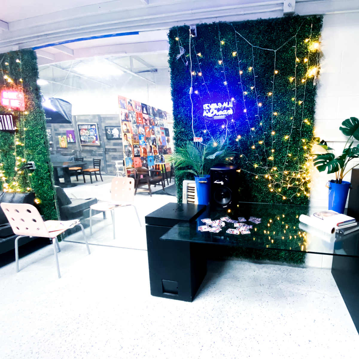 A modern workspace with a glass desk, an audio speaker, and a wall covered in greenery and string lights.
