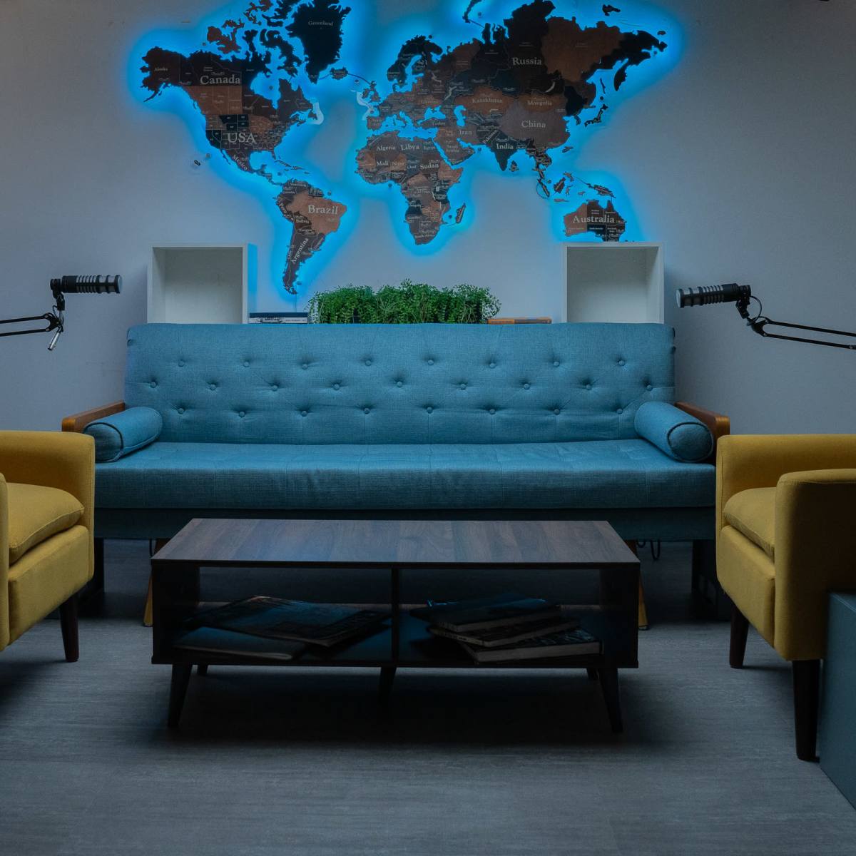 A modern seating area with a blue sofa, two yellow armchairs, a wooden coffee table, and a world map illuminated behind the furniture.