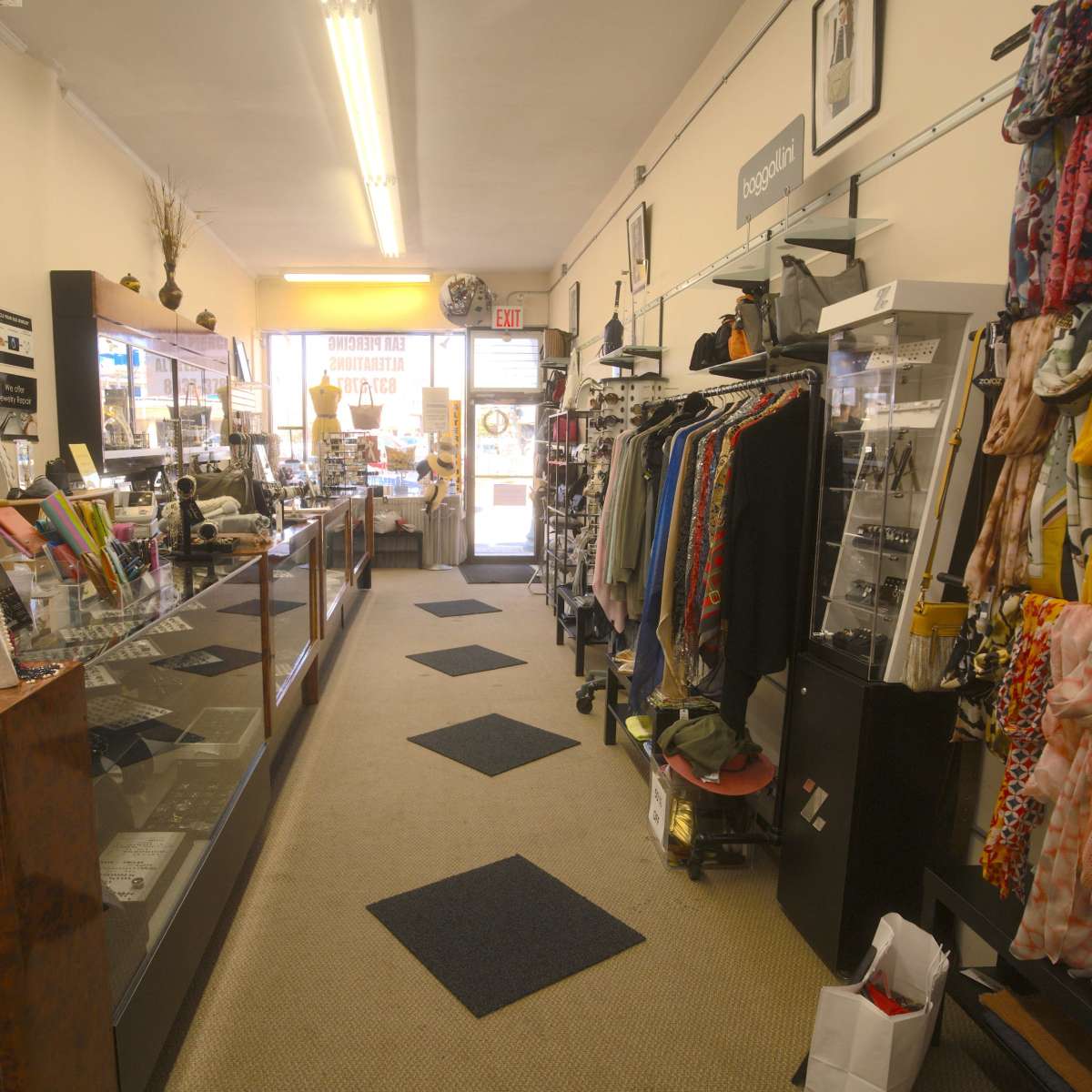 The interior of a retail store with displays of clothing and accessories along both sides of a narrow aisle leading to the entrance.