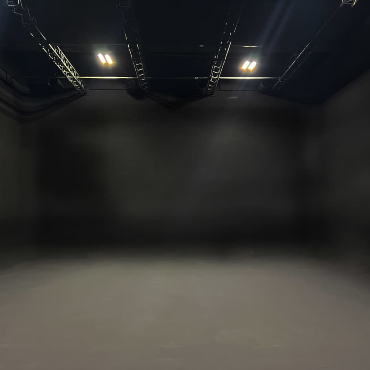 An empty black studio space with overhead lights and a seamless backdrop.