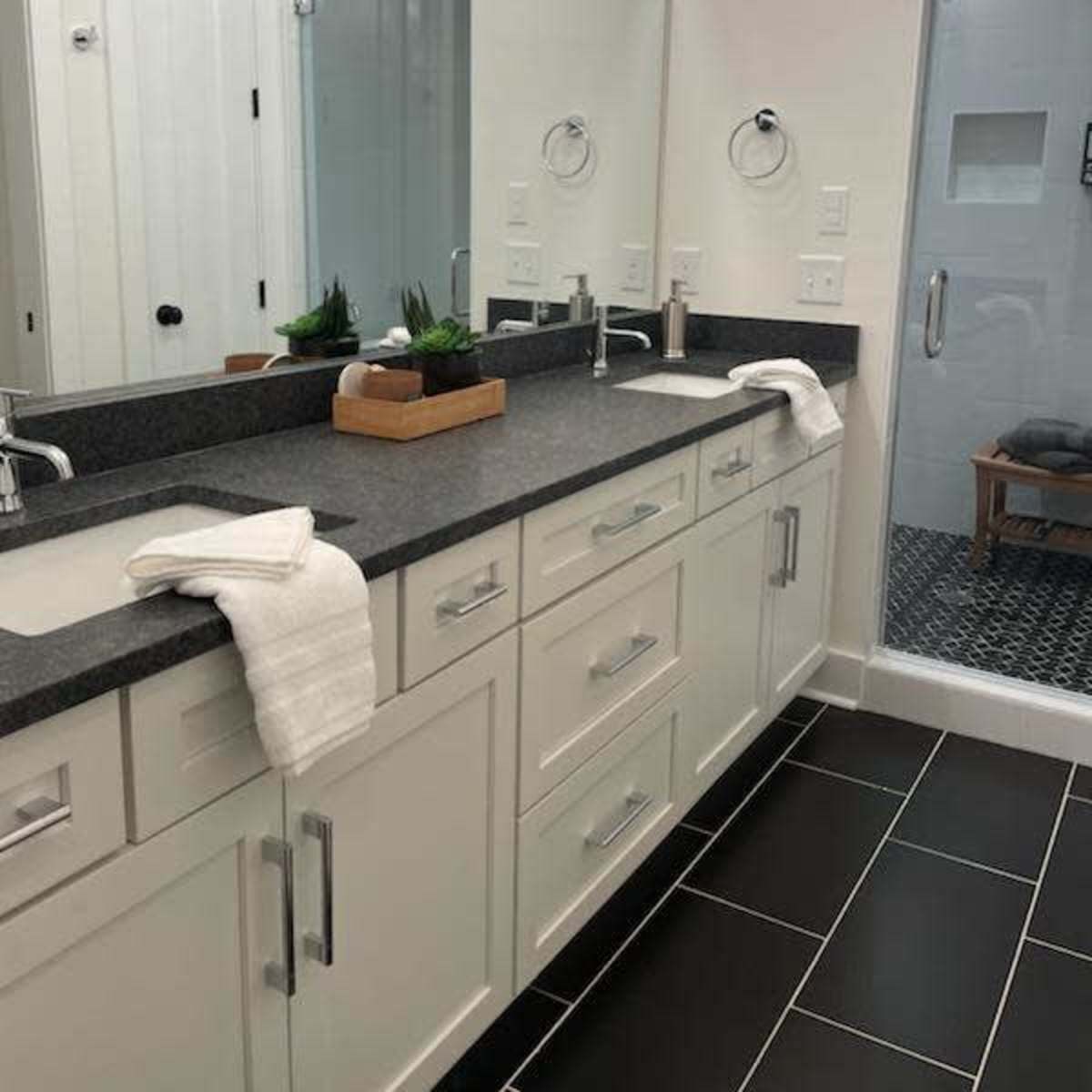 A modern bathroom with a double vanity featuring a dark countertop, white cabinets, and a glass shower enclosure.