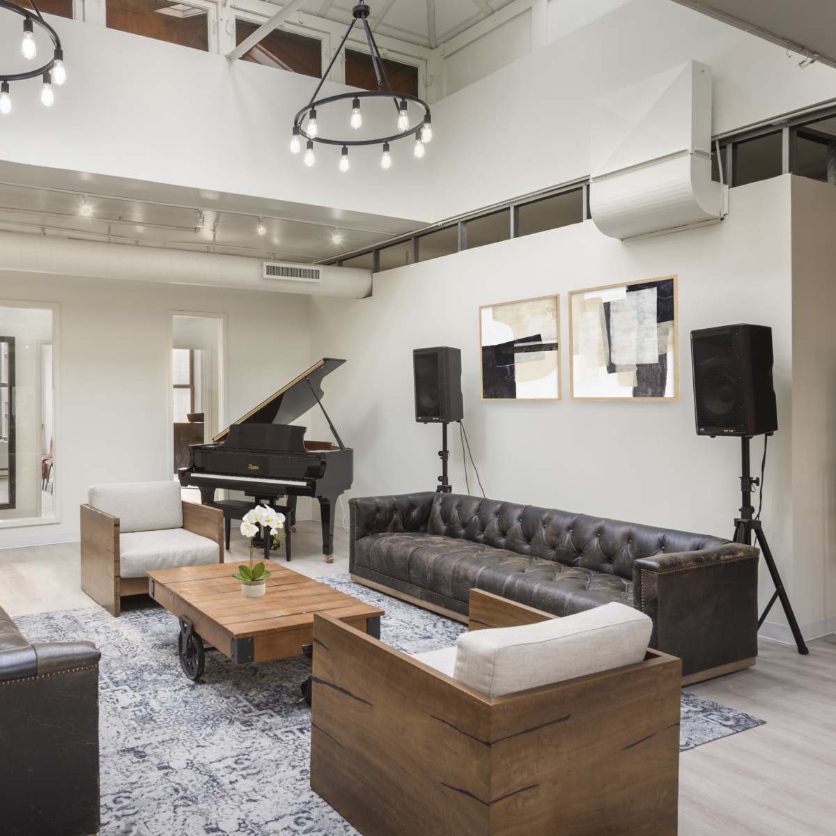 A modern lounge area with a grand piano, two leather sofas, a wooden coffee table with a vase of flowers, and large mirrors on the walls.