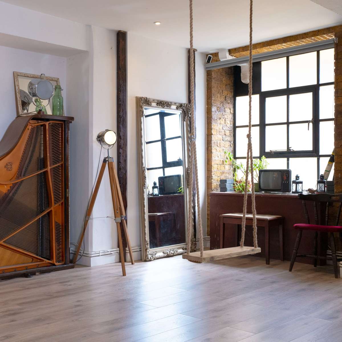 A spacious, well-lit interior features a grand piano against the wall, a floor lamp, a mirror, and a swing, with bookshelves and vintage decor.