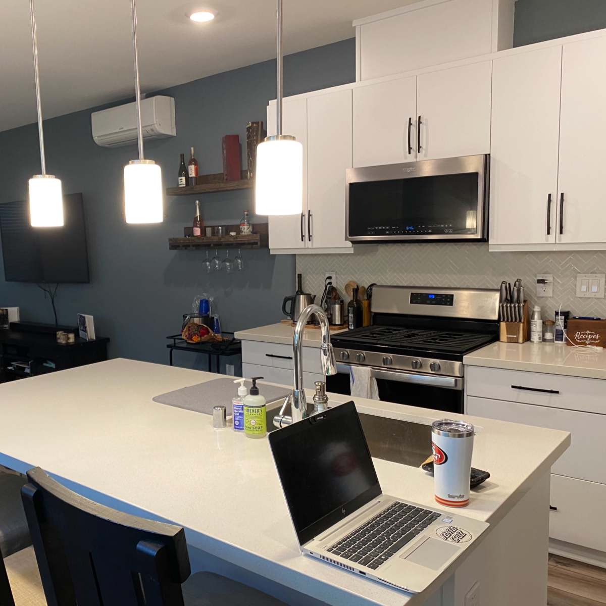 A modern kitchen features white cabinetry, a large island with bar seating, and a living area with a couch and television in the background.