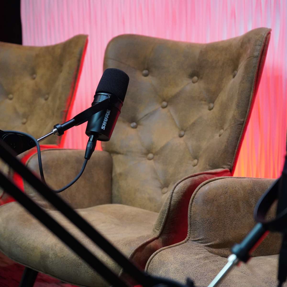 Two plush armchairs with microphones positioned in front of them, set against a softly lit, textured background.