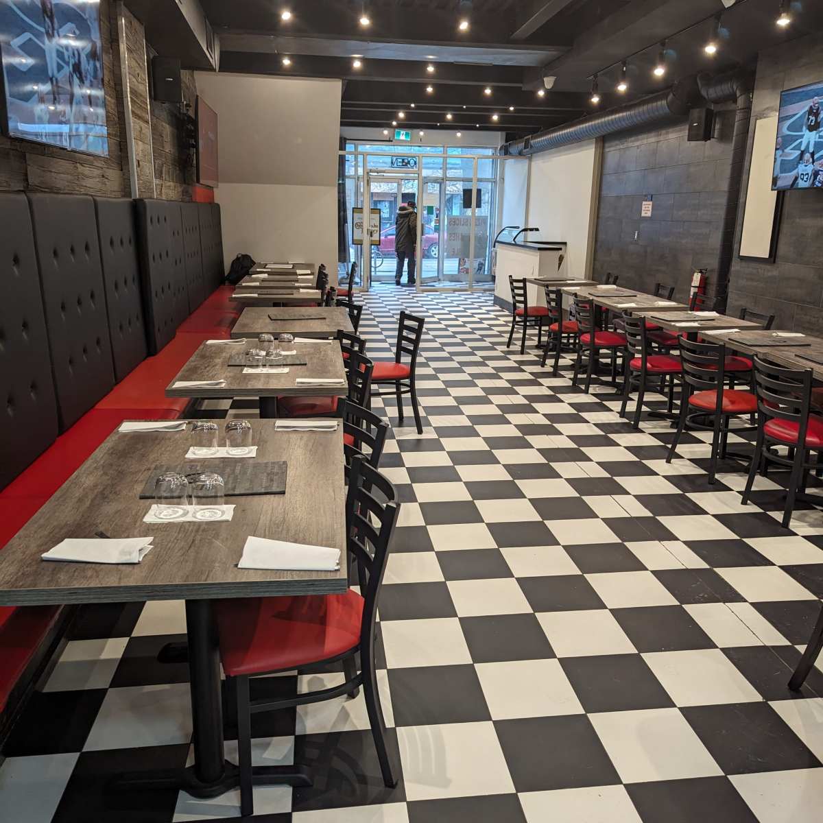 A restaurant interior with a black and white checkered floor, red upholstered seating, and multiple empty tables arranged in rows.