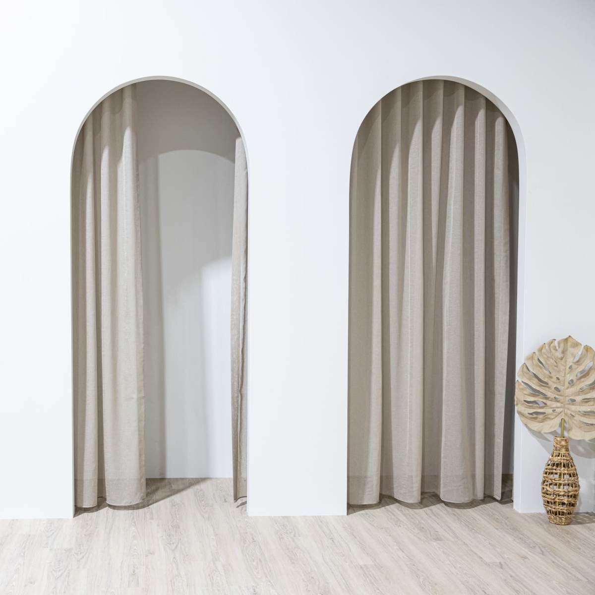 Three arched openings with neutral-colored curtains in a minimalist interior space.
