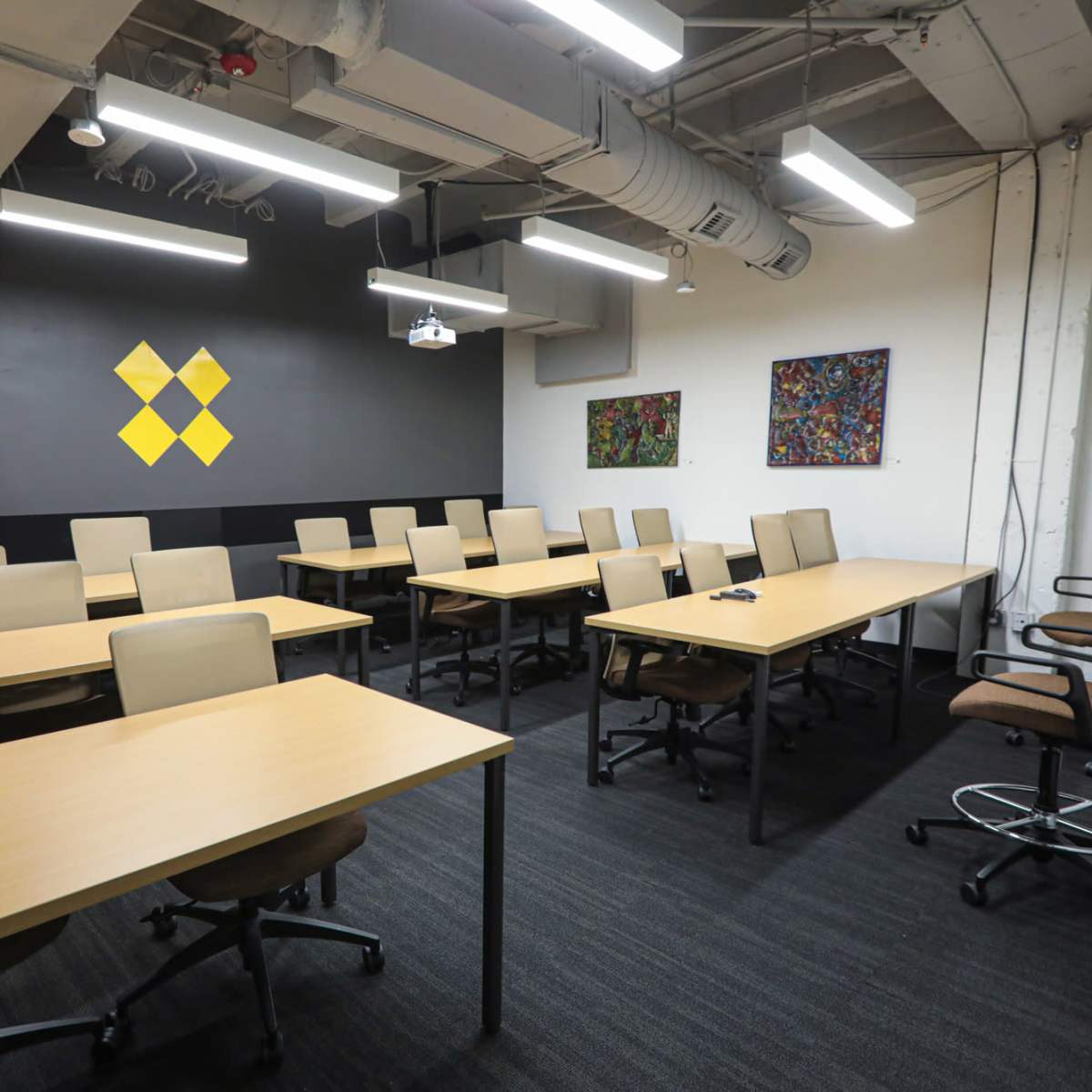 A modern meeting room with multiple rows of tables and chairs, and two artworks displayed on the wall.