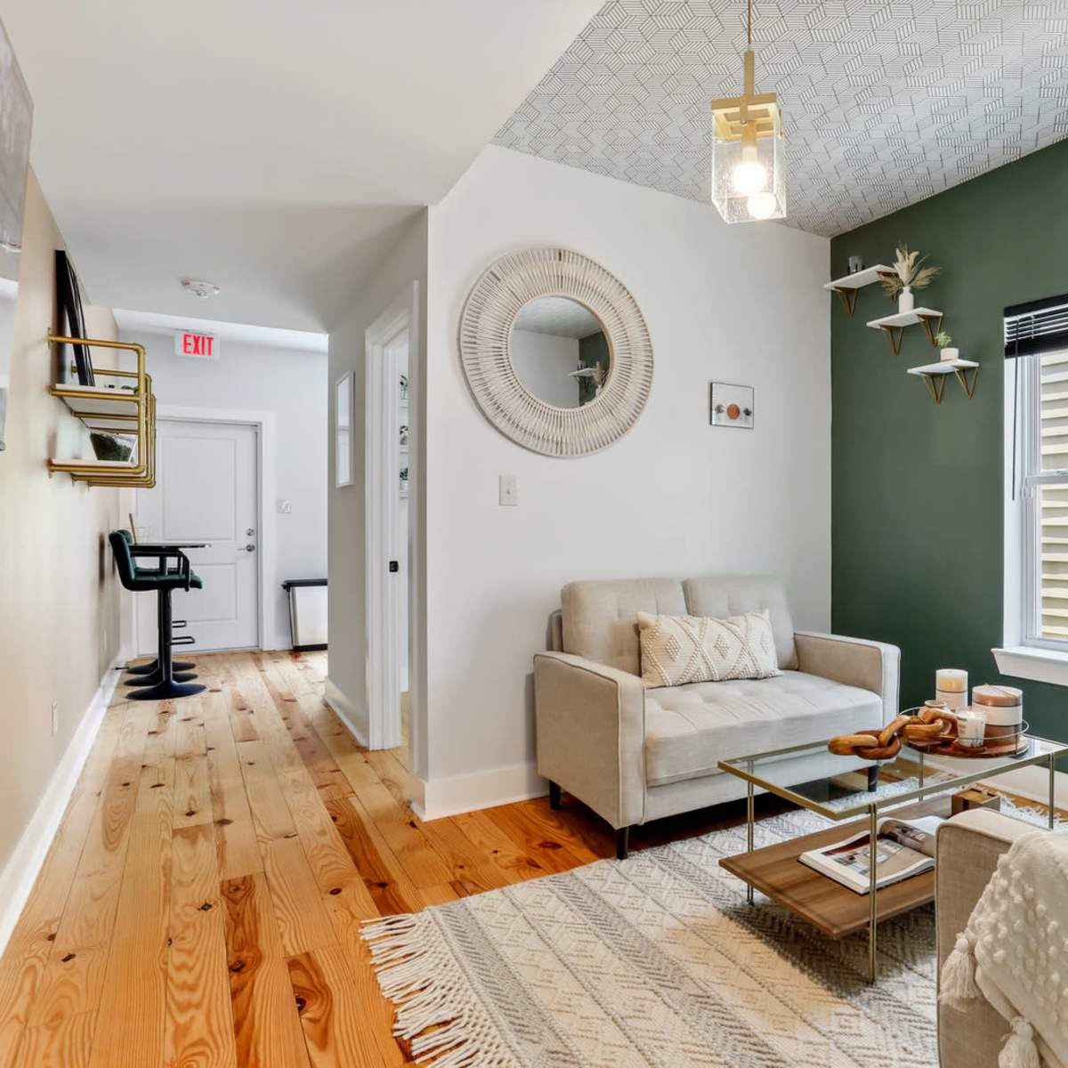 A living room features two light-colored sofas, a glass coffee table, and green accent walls, with decorative shelves and natural wood flooring.