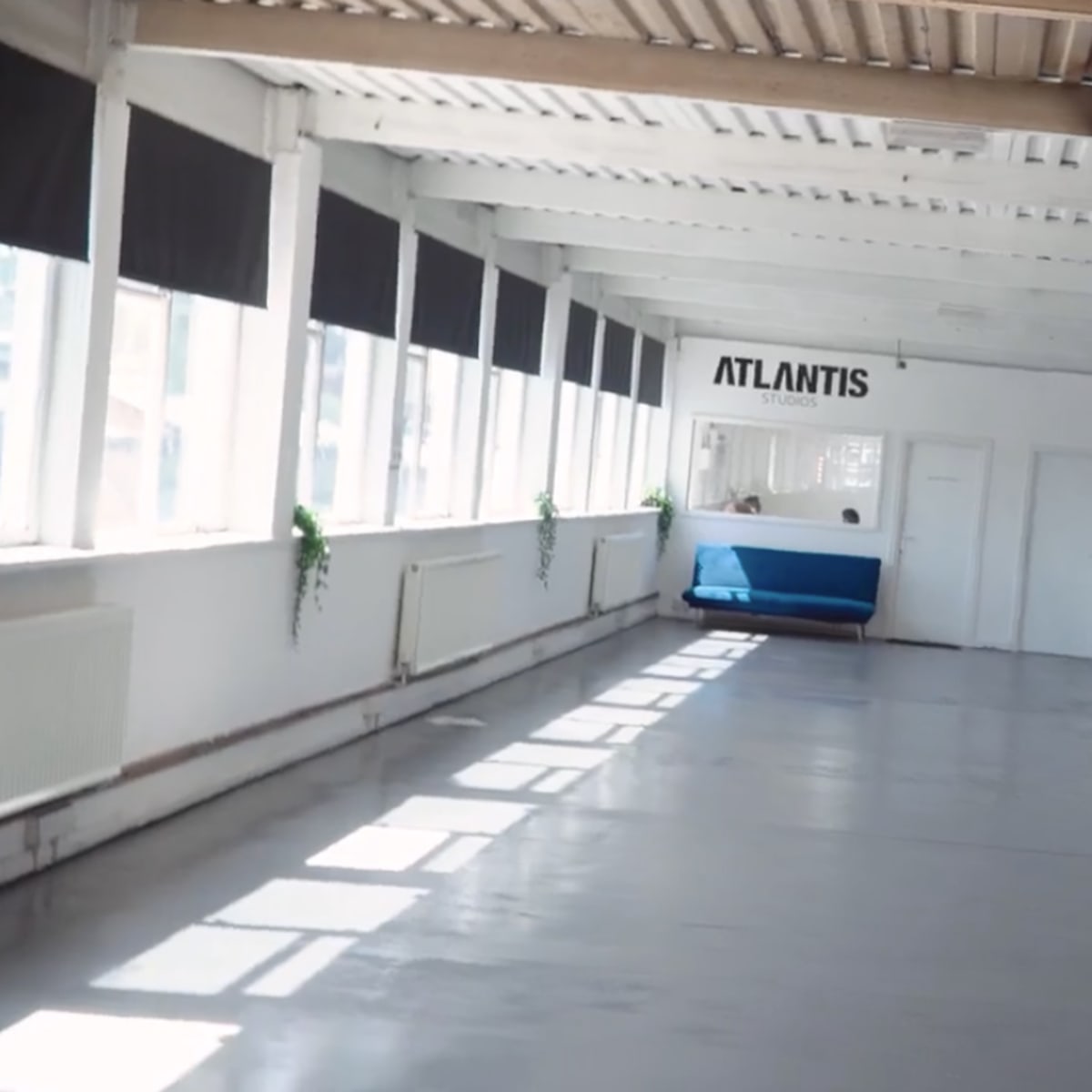 A bright, spacious interior with white walls, polished concrete flooring, and a blue object labeled "ATLANTIS" visible in the background.
