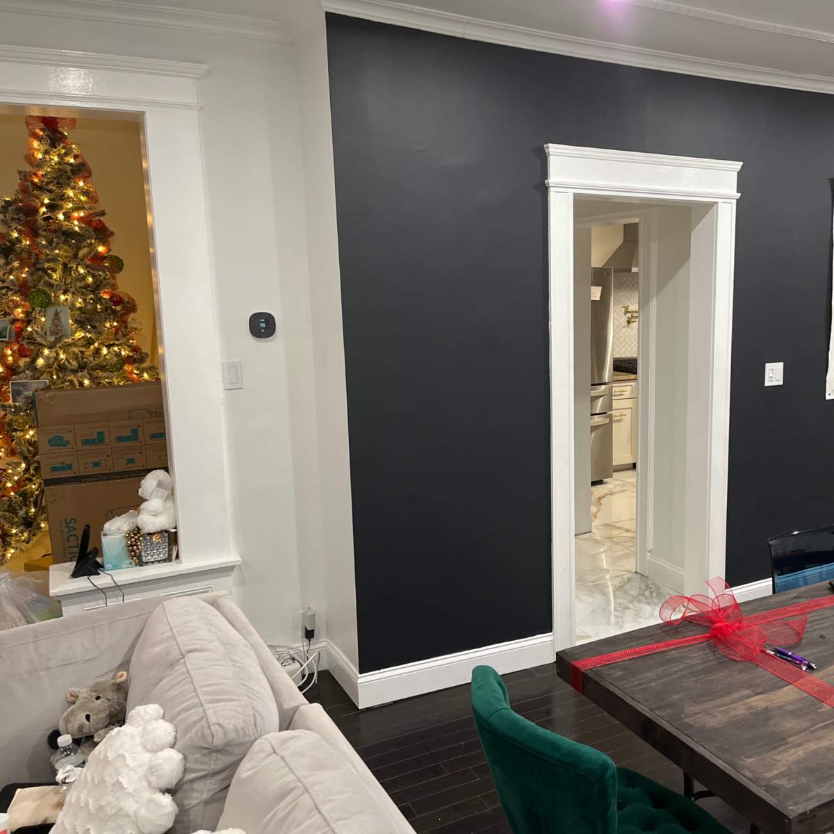 A dining area with a dark wall featuring an elephant painting, a dining table in the center, and a Christmas tree visible in the background.