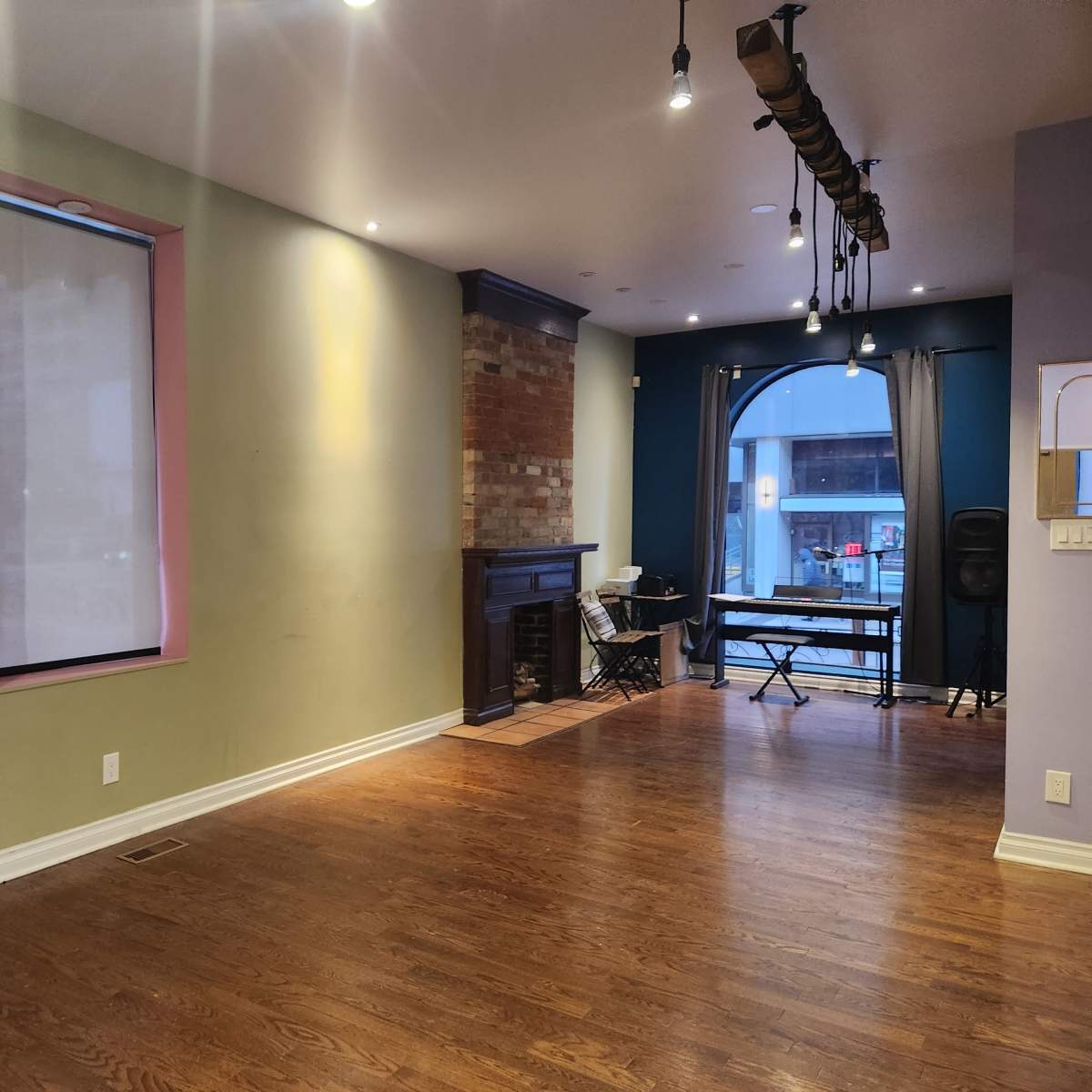 The room features hardwood flooring, two windows with shades, a brick fireplace, and a small table and chair set in an adjacent area.