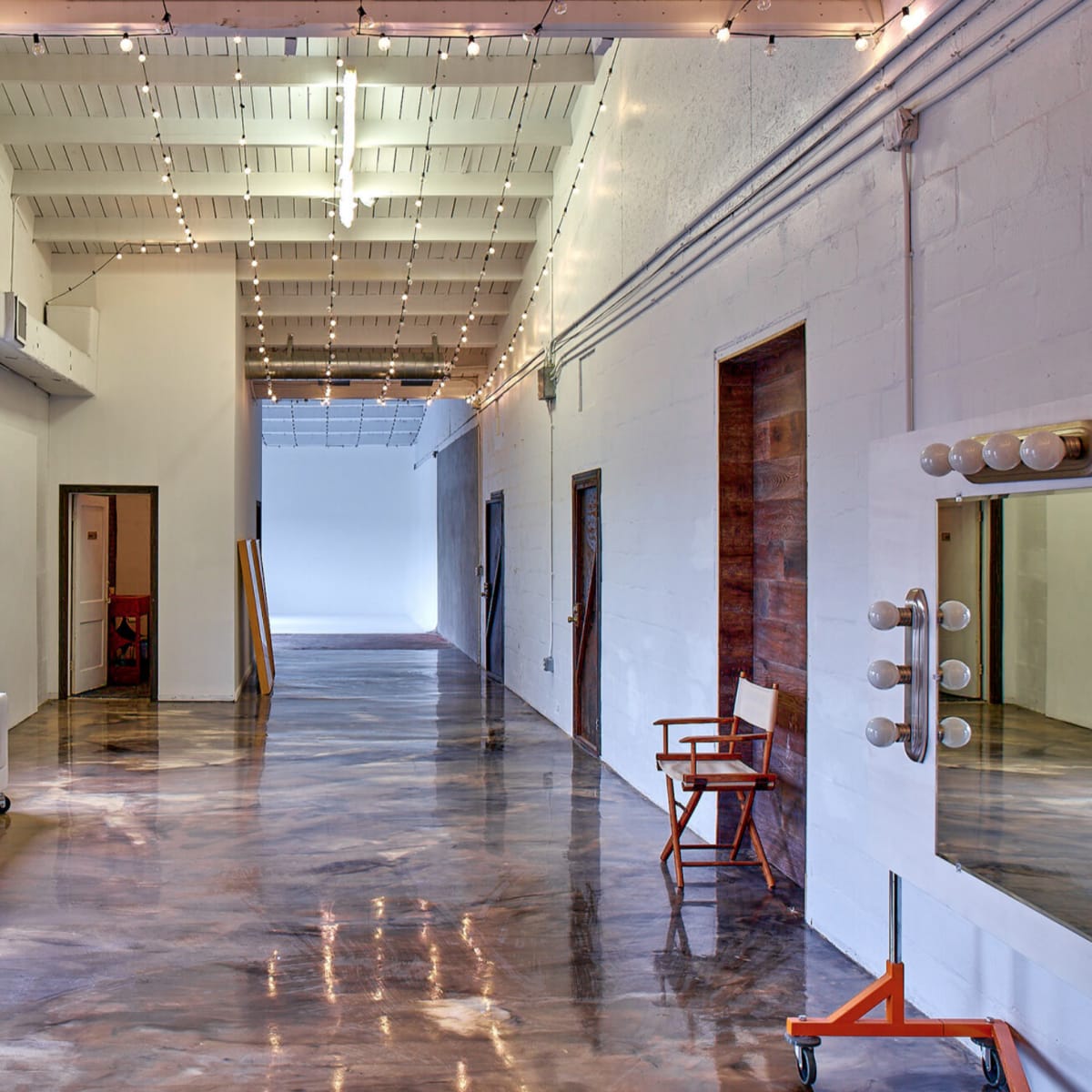 A spacious, well-lit interior corridor with polished concrete floors, large windows, and decorative string lights above.