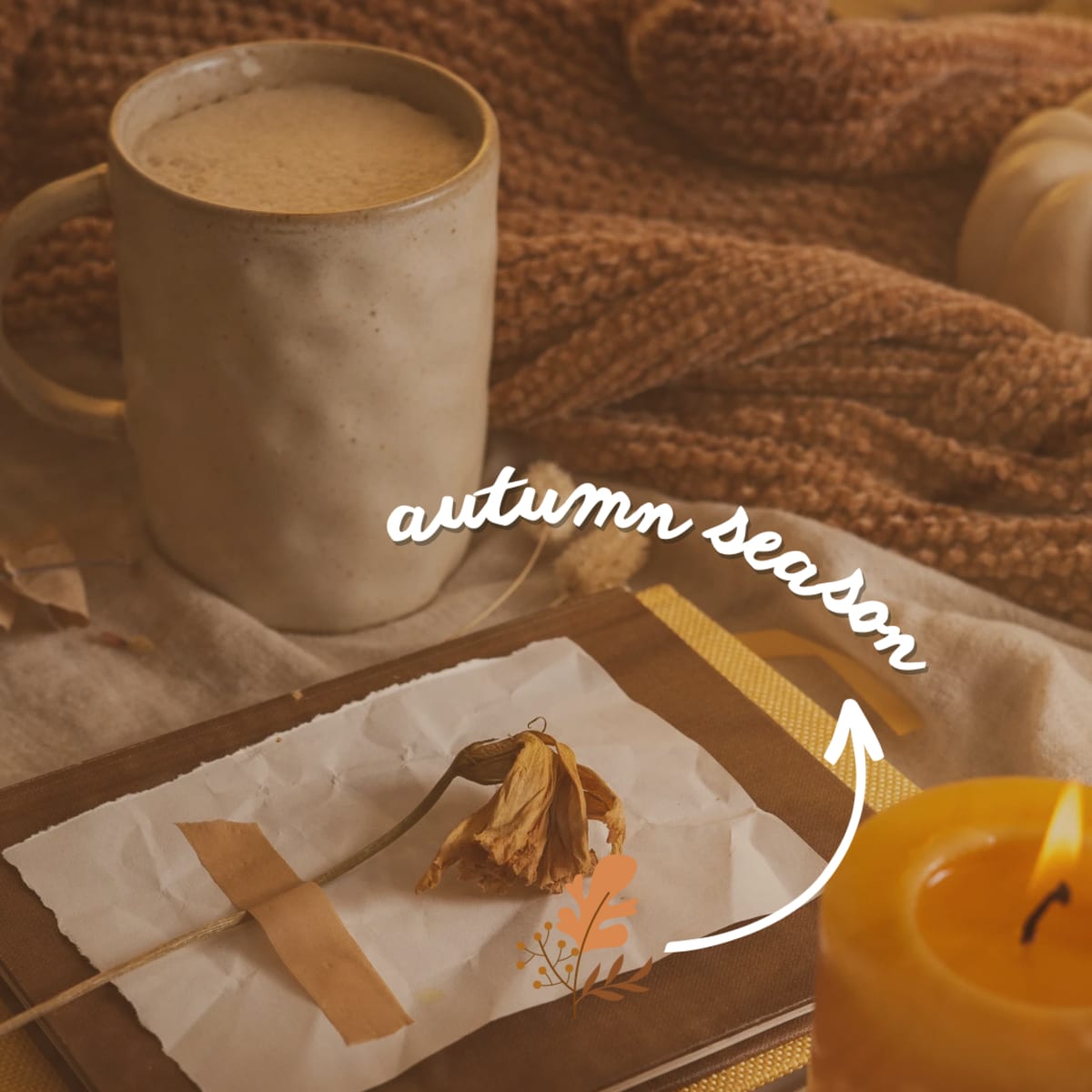 A cup of coffee sits next to a piece of paper with dried leaves, accompanied by a lit candle and a knitted scarf, evoking an autumn theme.