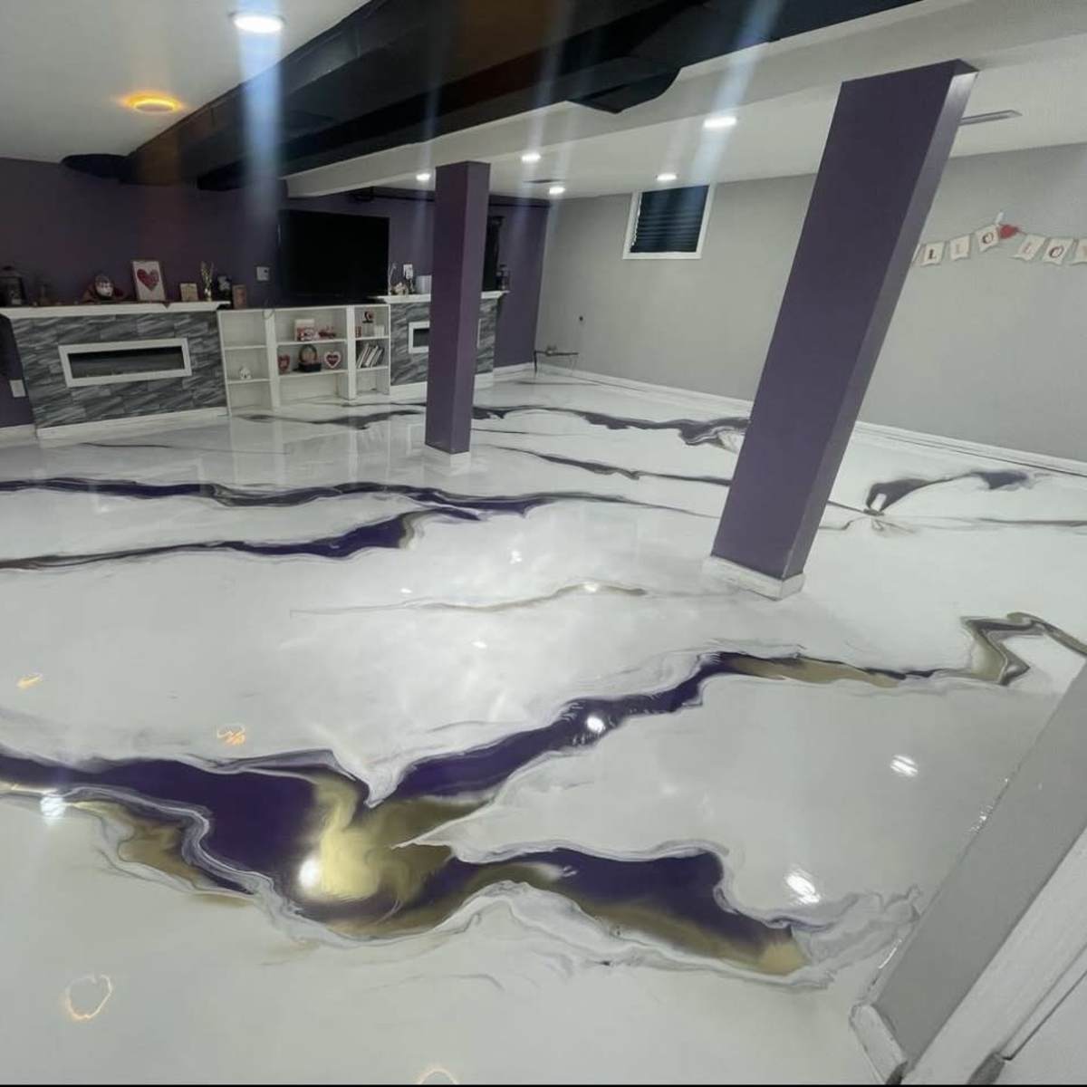 A basement with a glossy white floor featuring purple and gold marbled patterns, and purple walls with a shelving unit in the background.