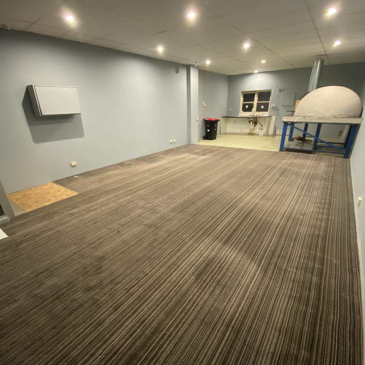 A spacious room with a carpeted floor, overhead lights, and a wall-mounted air conditioning unit.