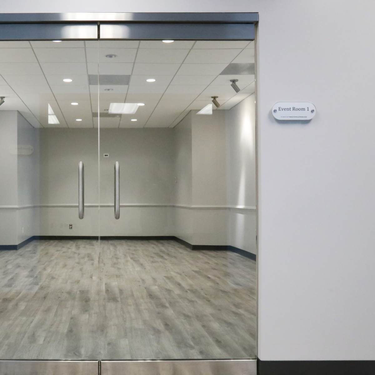 A glass entrance to an empty event room with grey walls and a wooden floor.