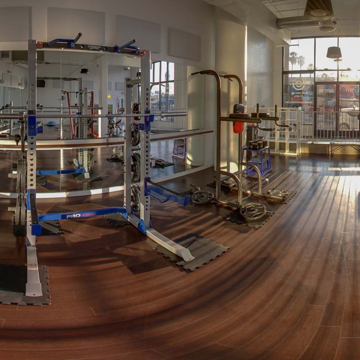 A spacious gym interior with various exercise equipment arranged on polished wooden floors.