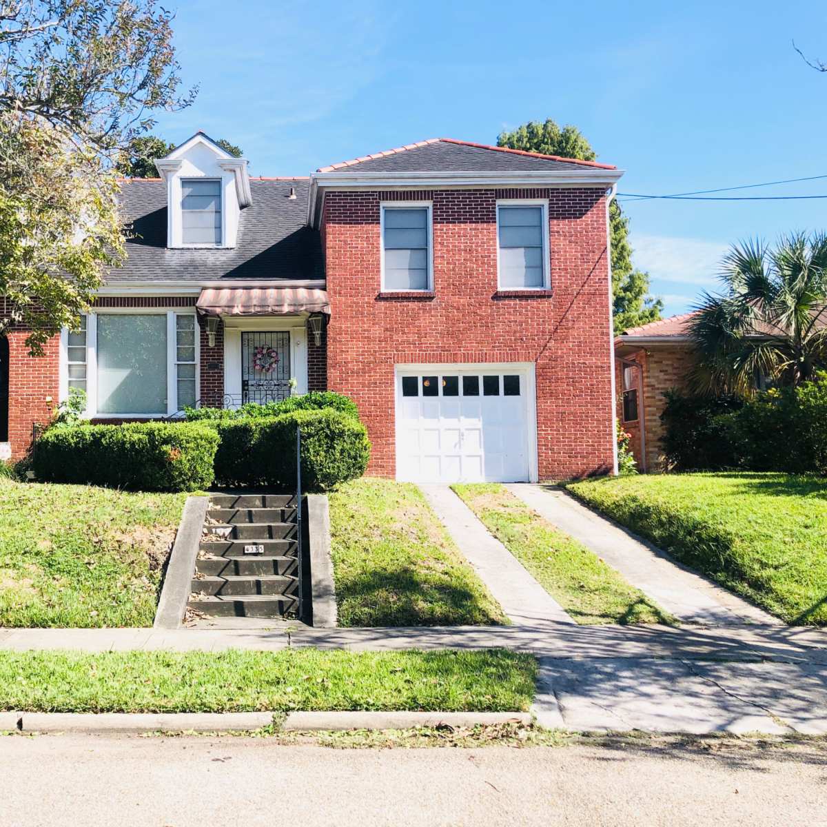 A two-story red brick house with a front garden and a driveway leading to a garage.
