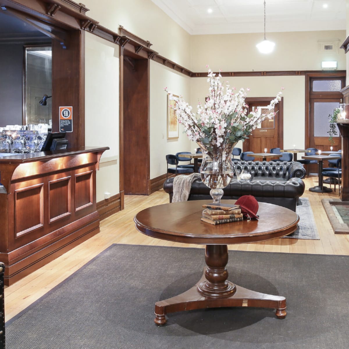 A lobby area featuring a round wooden table with a vase of flowers, surrounded by leather seating and a fireplace.