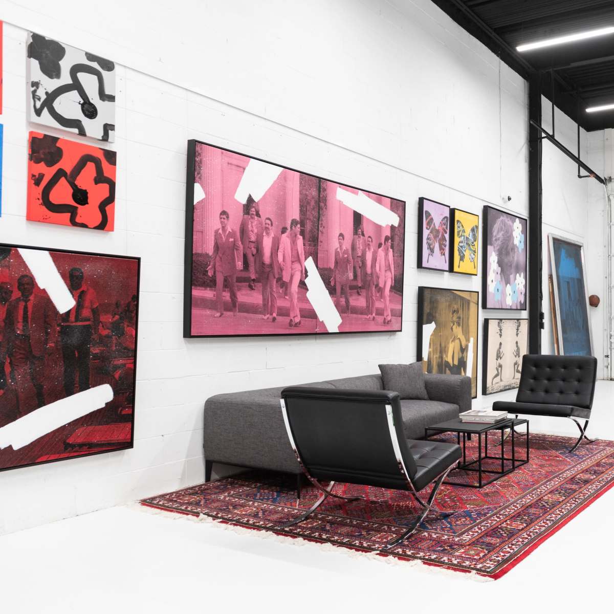 A spacious gallery with white walls featuring various framed artworks, a gray sofa, and a large area rug on a polished floor.