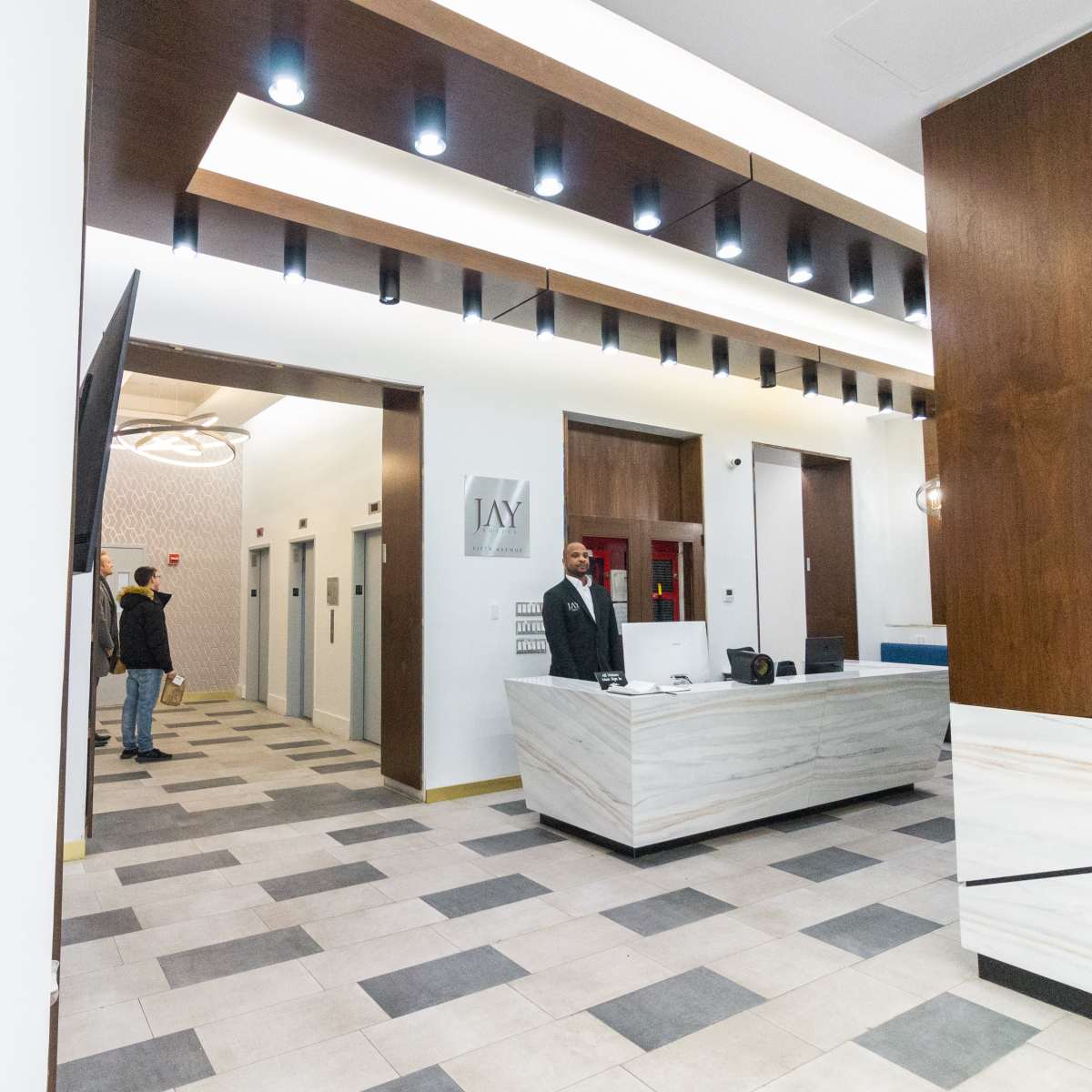 A modern lobby with a reception desk, elevators, and a security personnel standing by.