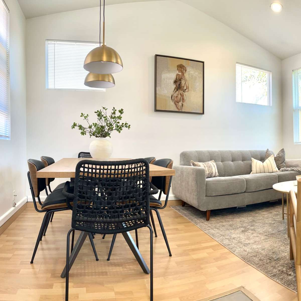 A modern living area with a gray sofa, a dining table surrounded by black chairs, and artwork on the walls.
