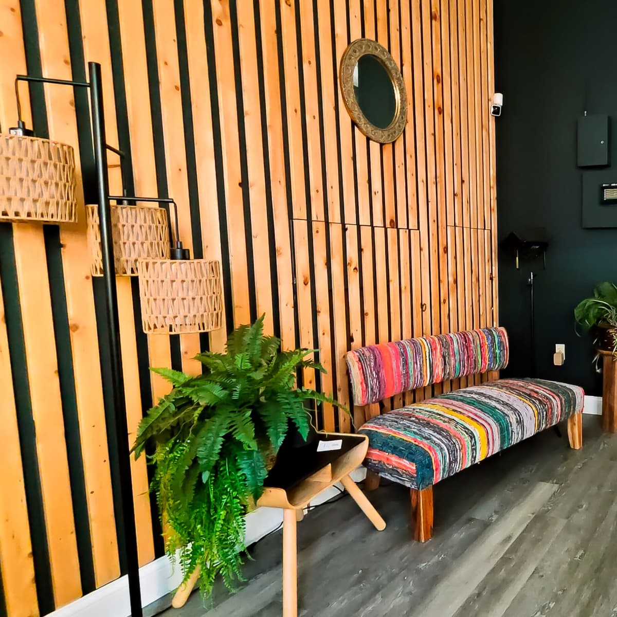 A modern interior space with wooden paneling, a colorful striped couch, plants, and an open area leading to another room.