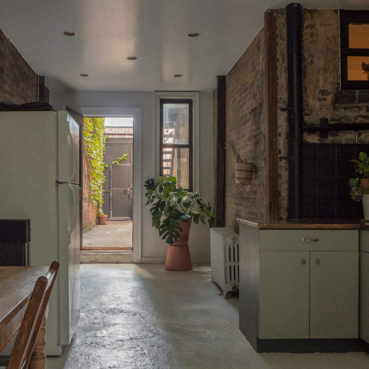 A spacious kitchen with a refrigerator, dining table, and a doorway leading to a backyard area.