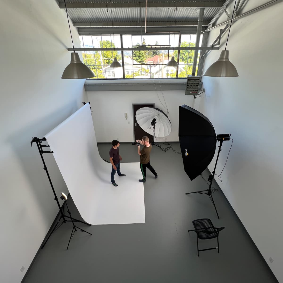Two people are standing on a studio backdrop while adjusting lighting equipment in a photography studio.