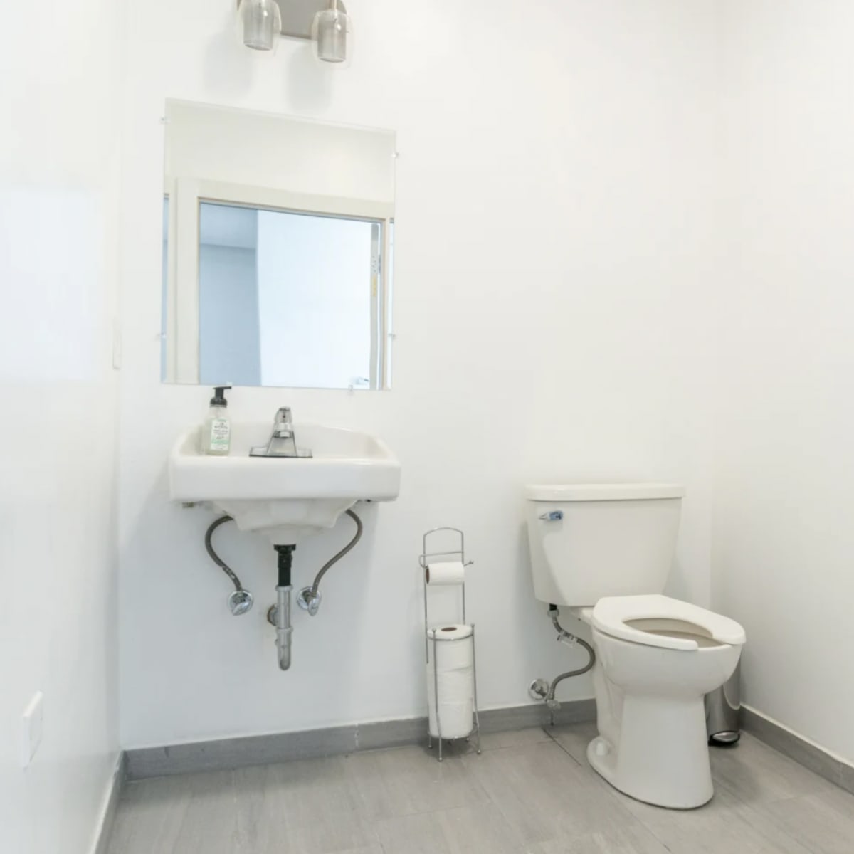 A small bathroom featuring a toilet, a sink with a mirror above it, and a roll of toilet paper on a holder.